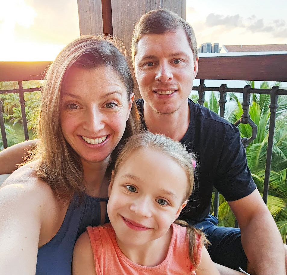 Family of three posing for a selfie on a balcony with greenery in the background